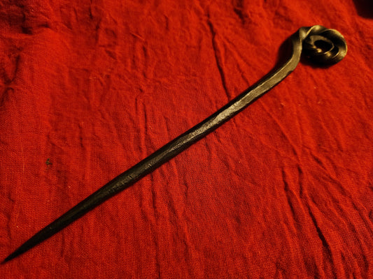 Dark metal hair pin with a spiral top on beige woven fabric.
