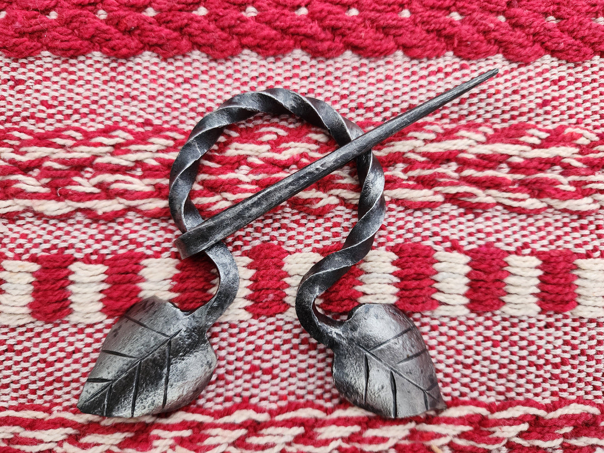Leaf-decorated blanket pin brooch fastening a grey cloak.