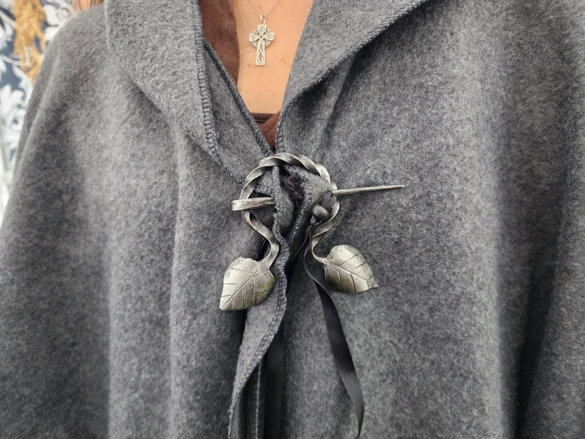 Close-up of a hand-forged leaf brooch on red and white woven fabric.