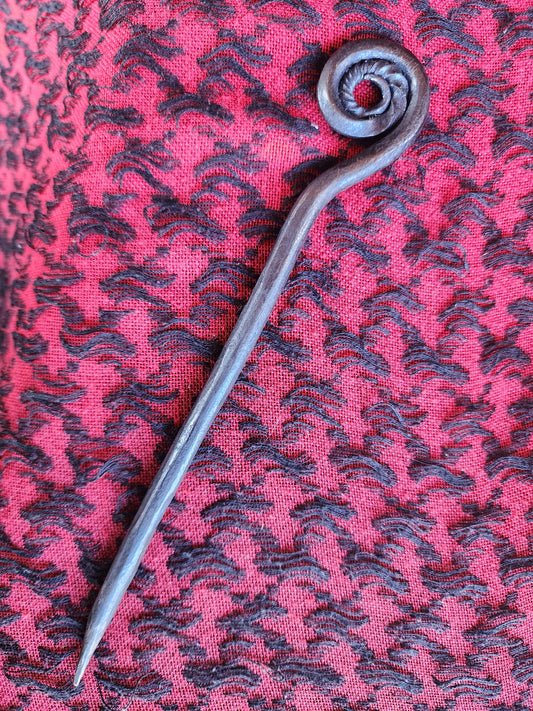 Metal hair pin with a curled spiral top on pink and black patterned fabric.