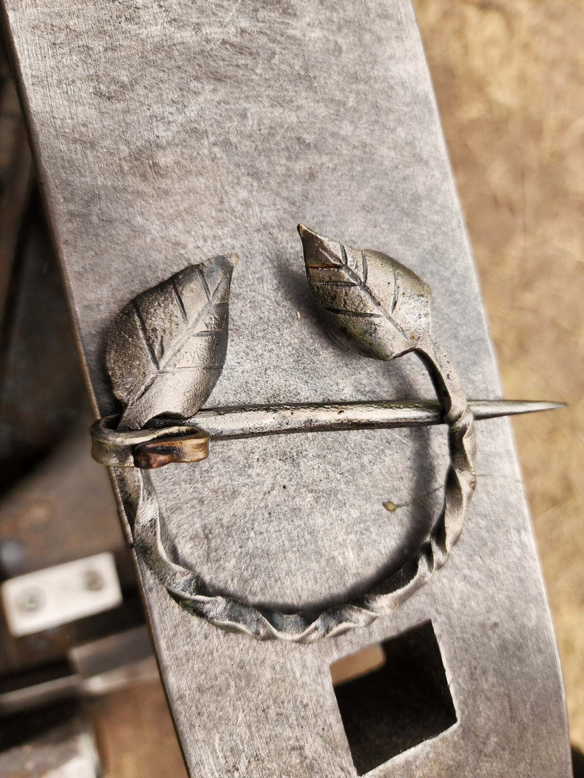 Hand-forged blanket pin brooch with two leaf details resting on an anvil.